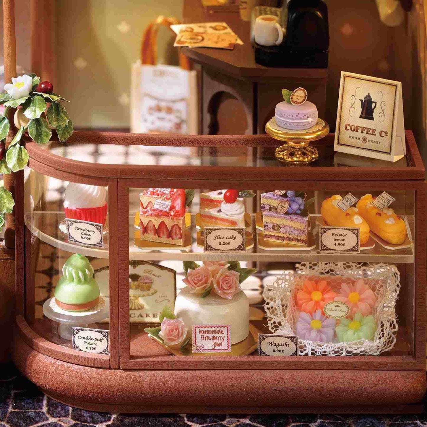 Miniature bakery display case with various pastries and a coffee cup on a wooden table.