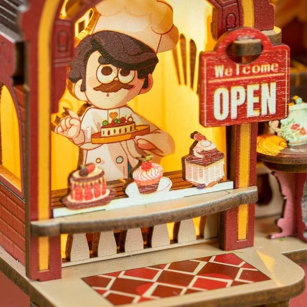 Wooden model of a dessert pickup counter with a character in a chef's outfit and 'Open' sign.