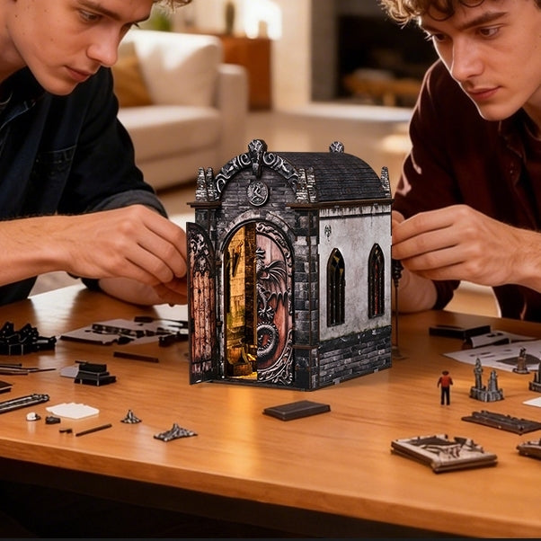 Two people assembling a detailed book nook model of a gothic-style dragon castle building on a wooden table.