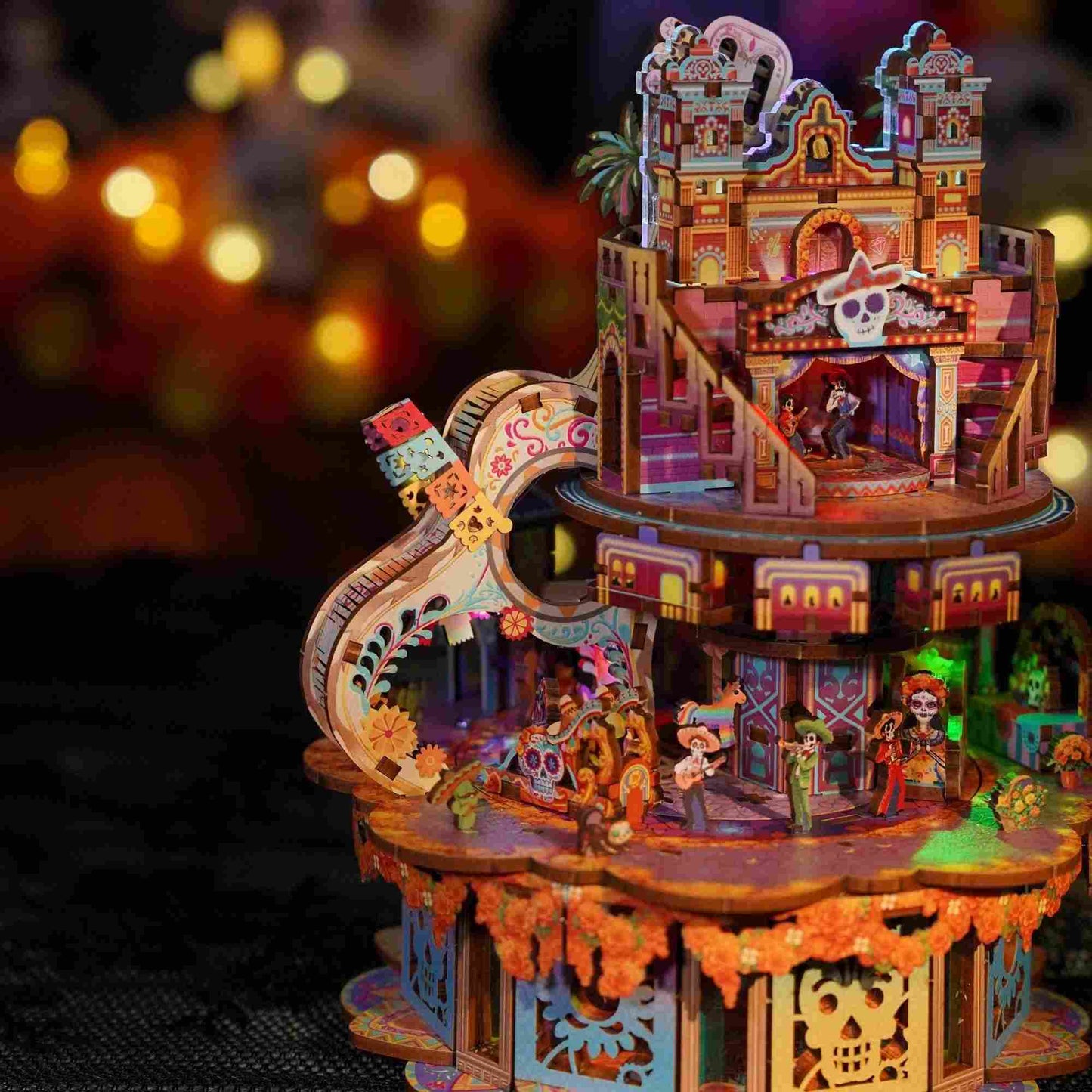 music box model of a Coco-Inspired festive scene with people and buildings, illuminated against a blurred background.