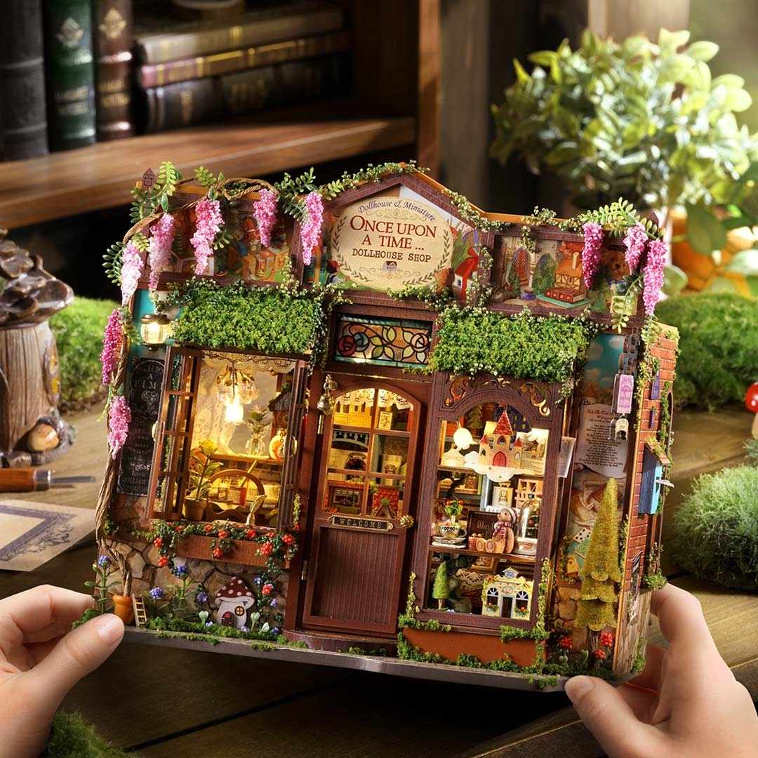 Miniature fairy tale shop model held by hands with a cozy indoor background
