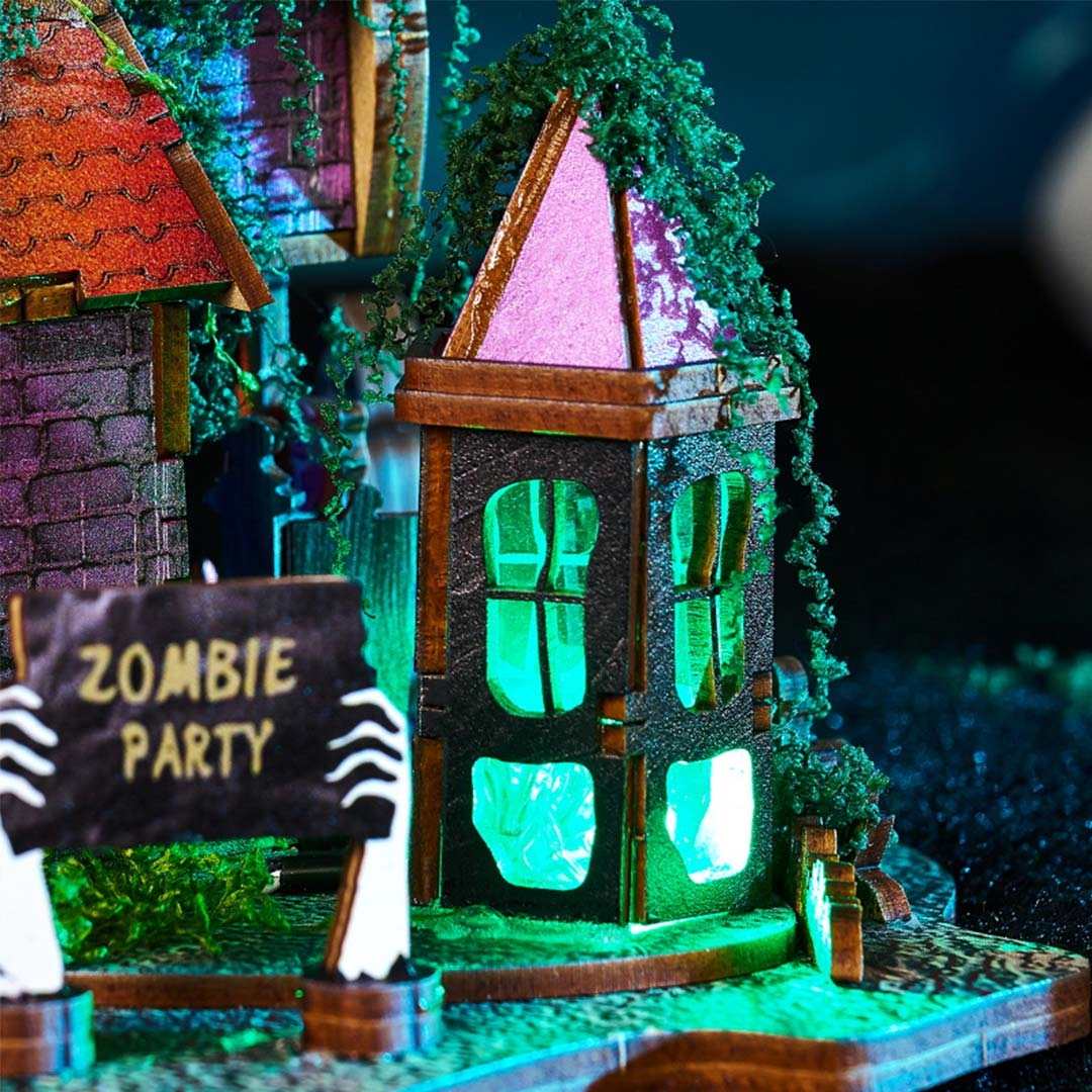 Halloween-themed miniature haunted house with zombie hand holding a 'Zombie Party' sign, illuminated with green lights.