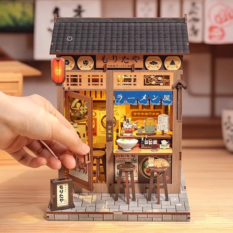 Miniature house model of a Japanese ramen shop with a hand opening the door.