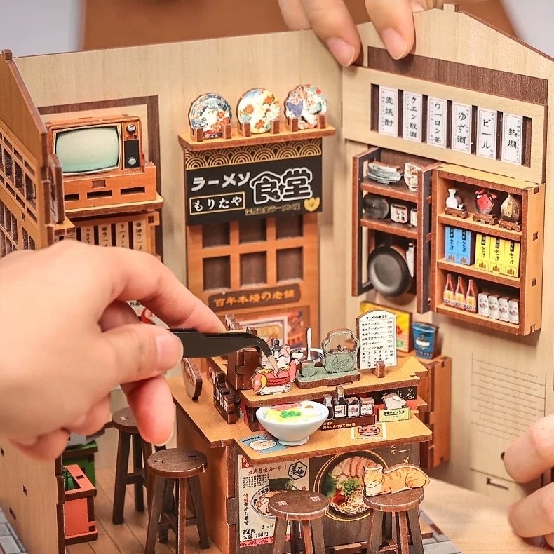 Miniature model of a Japanese restaurant with detailed interior and hand putting the miniature cat on the counter