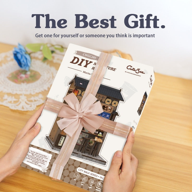 Gift box of Japanese Ramen Shop DIY Miniature House Kit with a bow held by hands, with text 'The Best Gift.