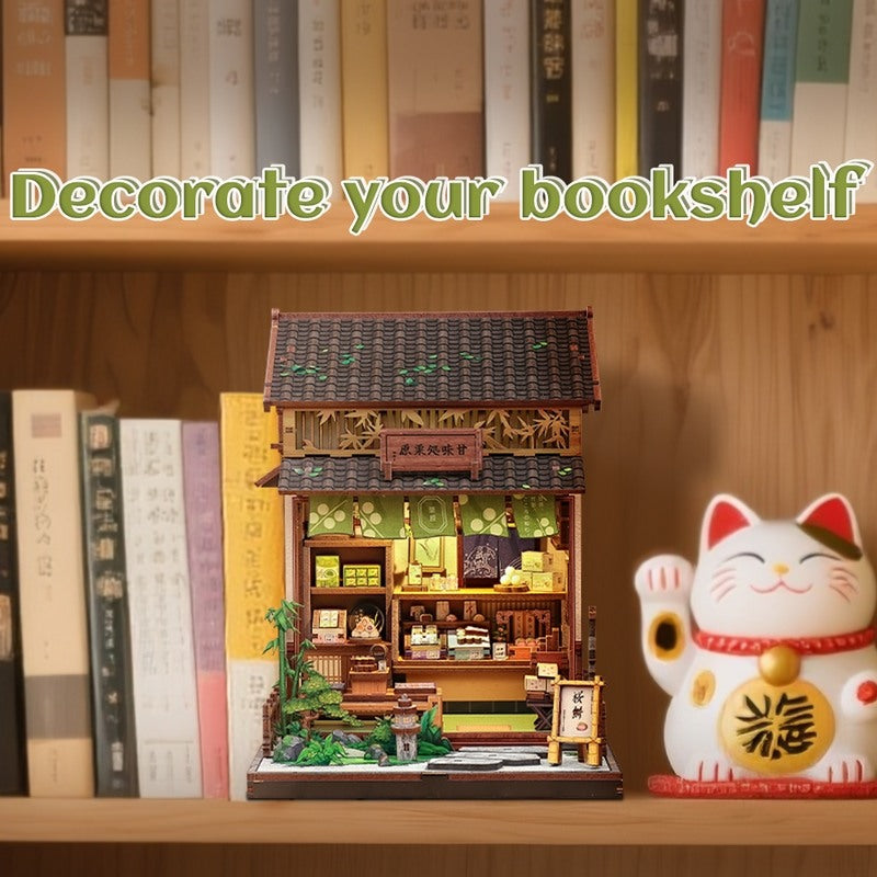 Miniature house model of a traditional Japanese sweet shop building on a bookshelf with a Maneki Neko figurine.