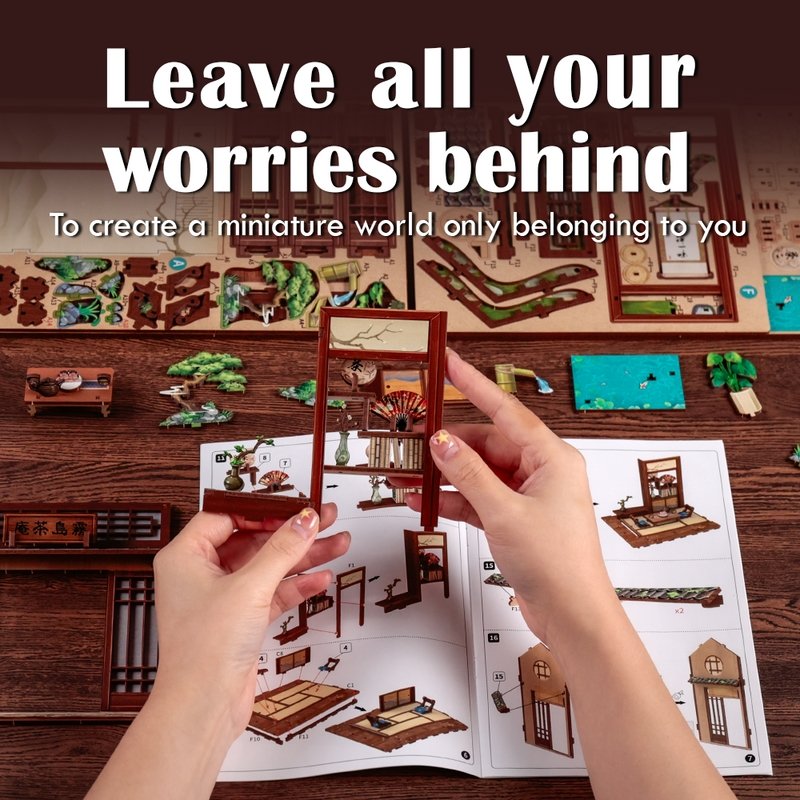 Hands assembling a miniature model kit with text 'Leave all your worries behind' on a wooden surface.