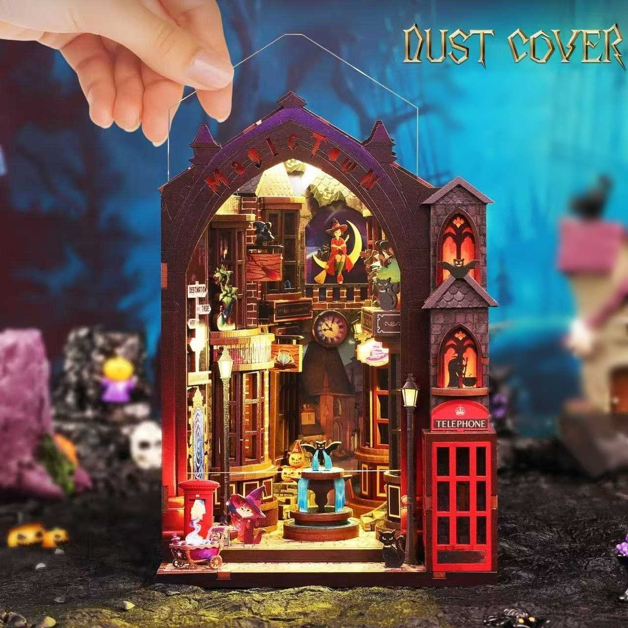 Hand holding a dust cover over a detailed book nook model of a magic gothic-style room with various objects.