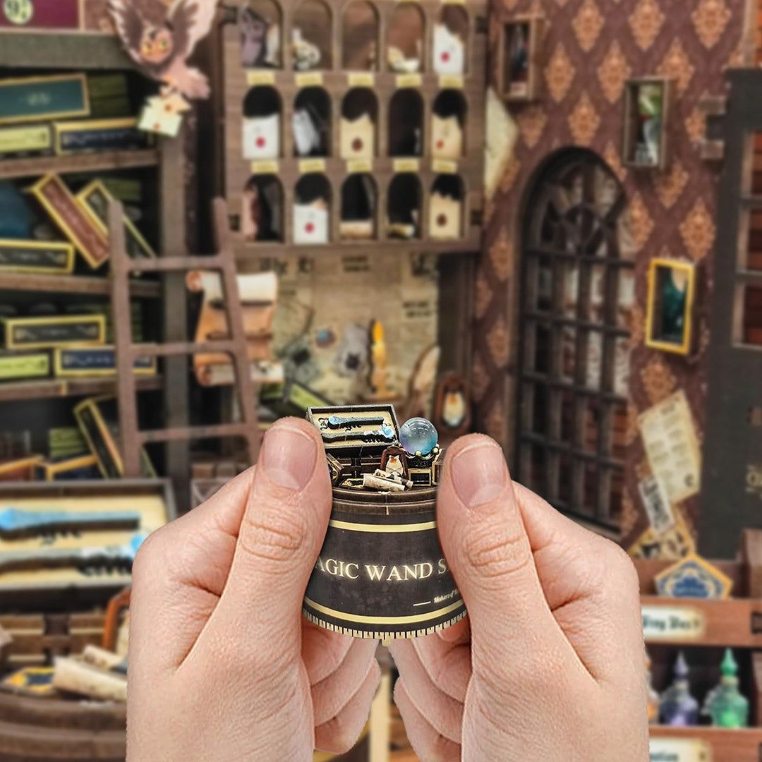 Hand holding a small, intricate model of a wand with a glowing tip against a detailed background.