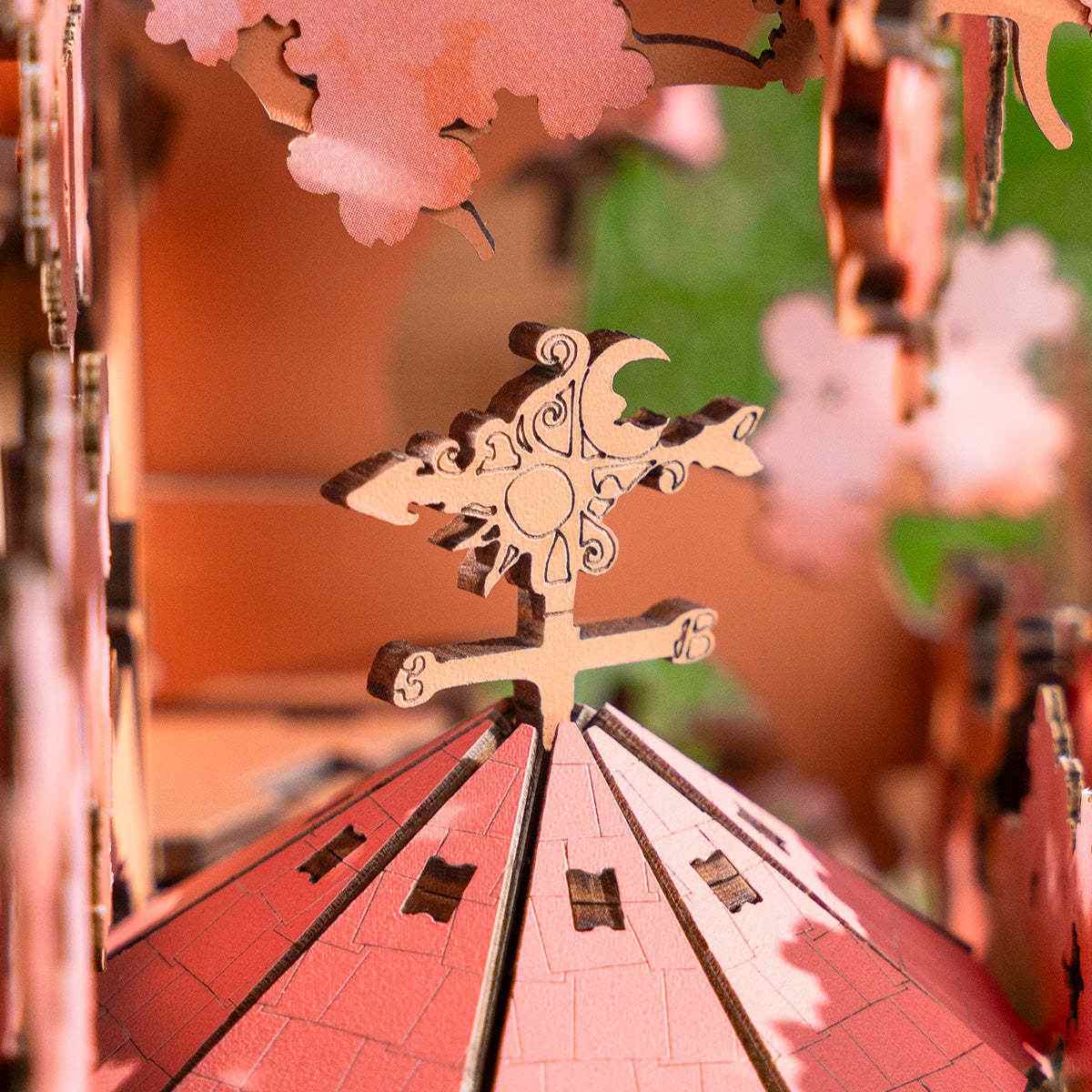 Close-up of a decorative wooden weather vane with intricate carvings and pink cherry blossoms in the background.