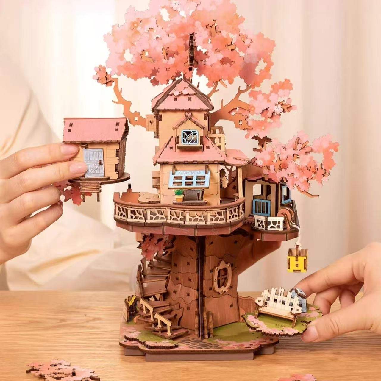 Wooden puzzle model of a treehouse with cherry blossoms, being assembled on a wooden table.