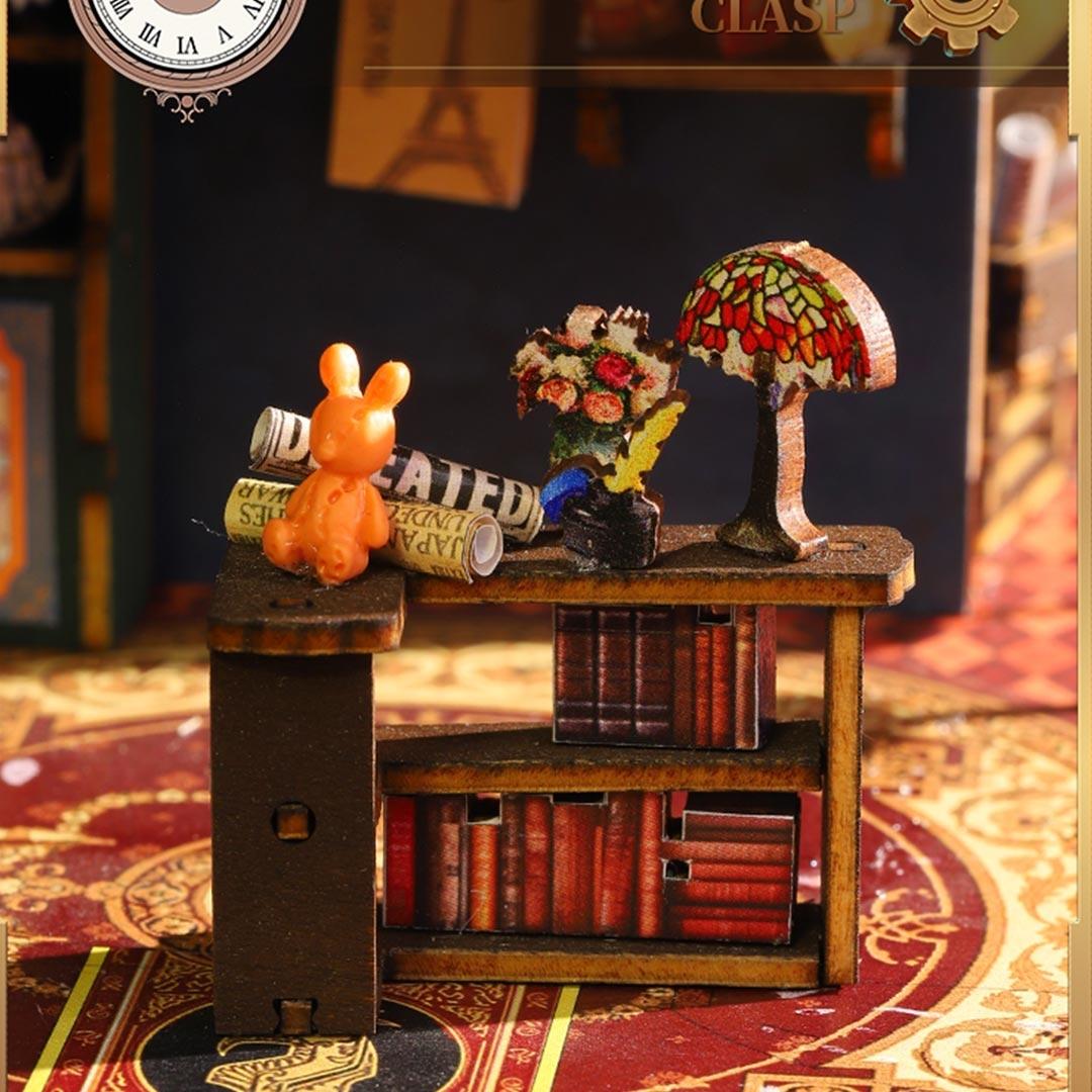 Miniature desk scene with books, lamp, and rabbit figure on a decorative surface.