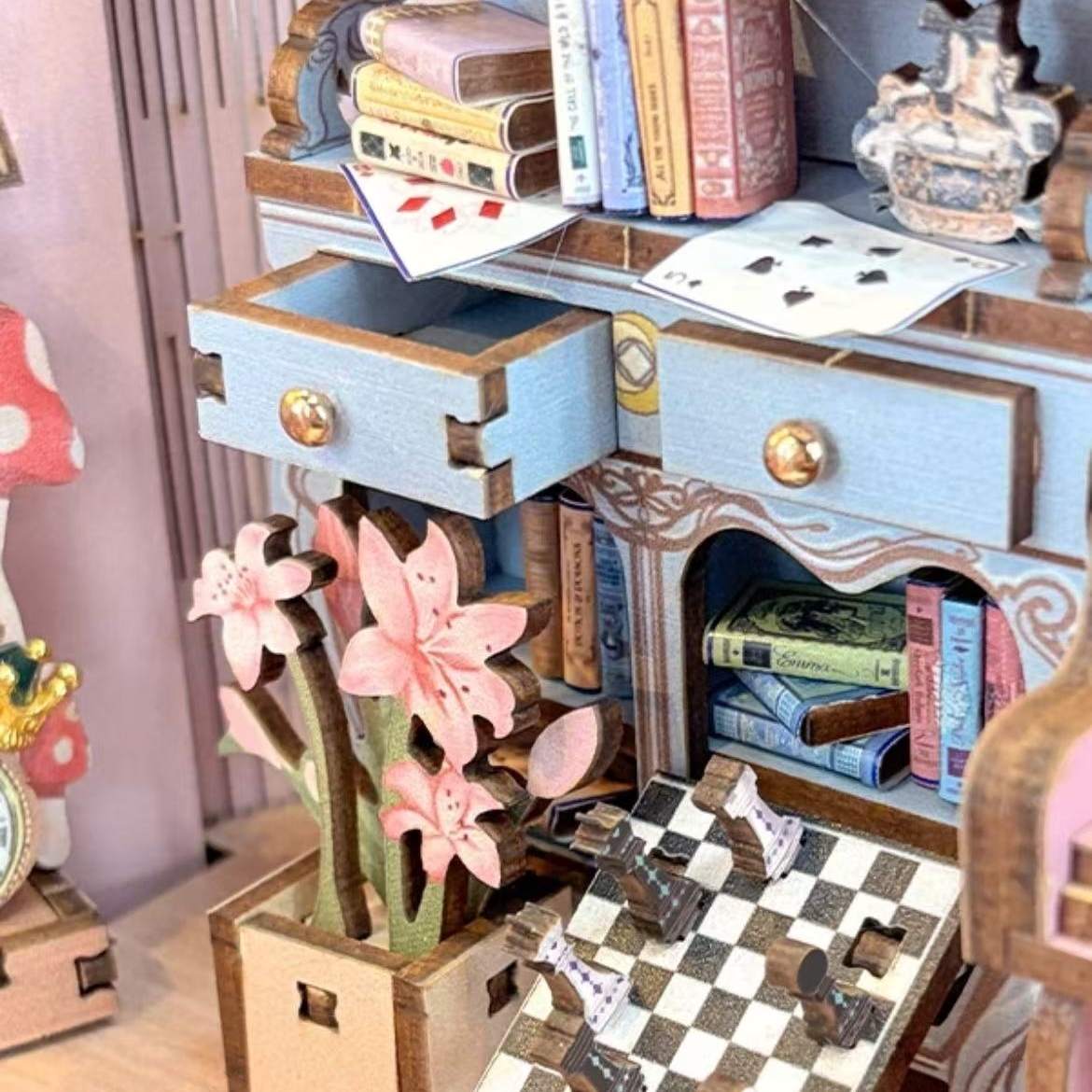 Miniature wooden desk with drawers, books, and decorative items on a checkered surface.