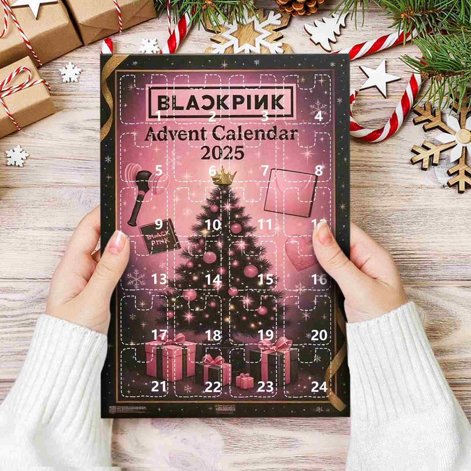 Blackpink 2025 Advent Calendar held by hands on a wooden surface with Christmas decorations.