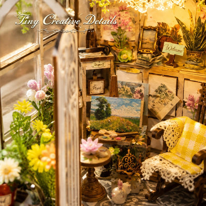 A miniature dollhouse interior scene with a cozy room setup, including a small yellow-and-white checkered chair, lace-covered cushions, a painted landscape canvas, floral arrangements, and vintage-style decor. The text 'The Tiny Creative Details' appears across the top.