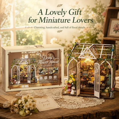 A miniature floral greenhouse gift set displayed on a wooden table, with the assembled decorative greenhouse on the right and its retail box on the left. The scene includes soft floral background elements, lace cloth, and overlaid promotional text reading 'A Lovely Gift for Miniature Lovers' and 'Demi's Flower House.