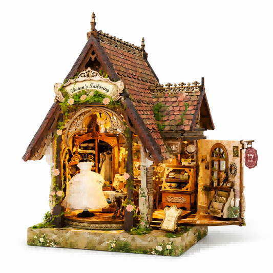 A miniature dollhouse-style boutique building with a pitched roof, warm amber interior lighting, floral greenery, and an open side door revealing a detailed shop interior. The front sign reads "Vivian's Tailor's".