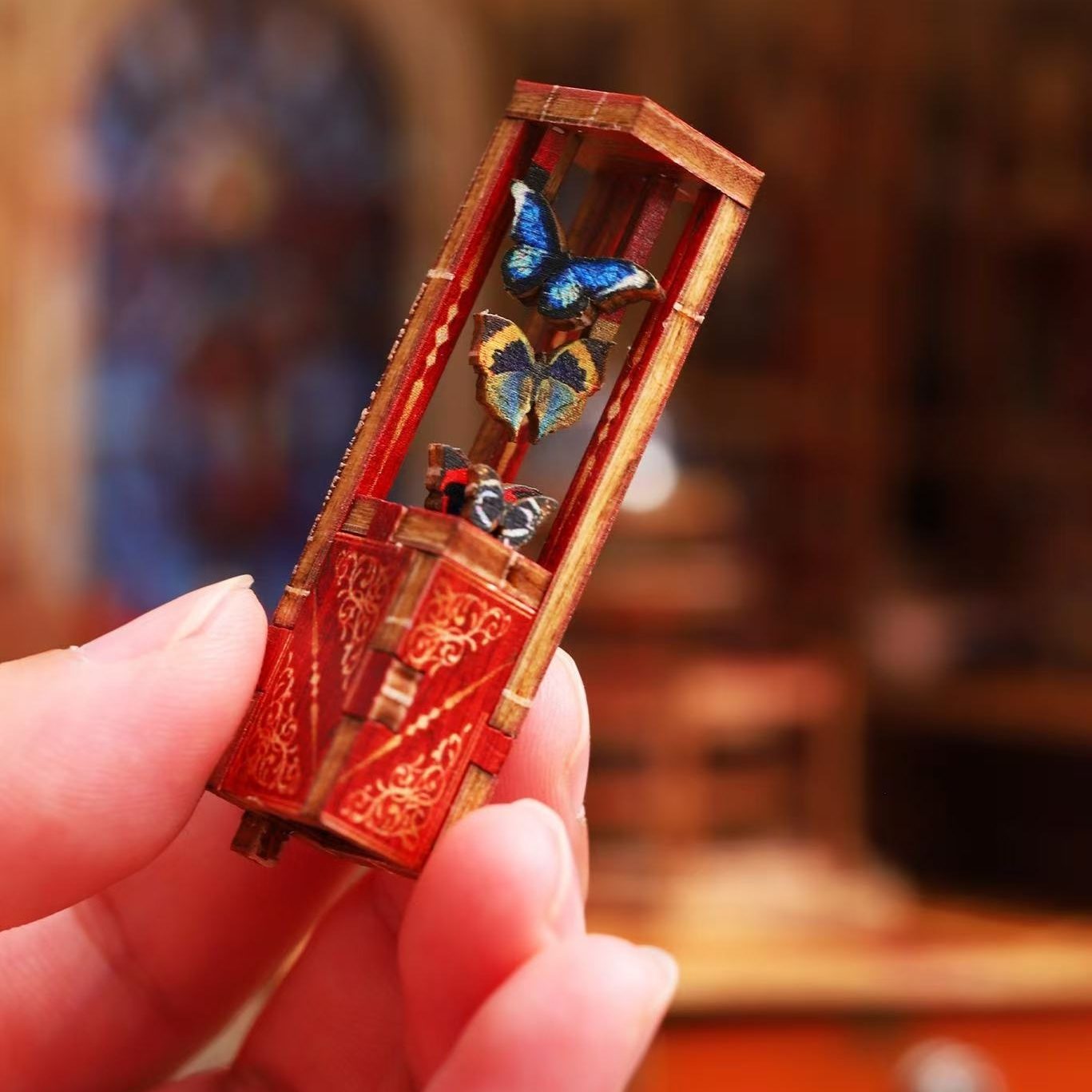Miniature wooden box with butterfly design held by a hand against a blurred background