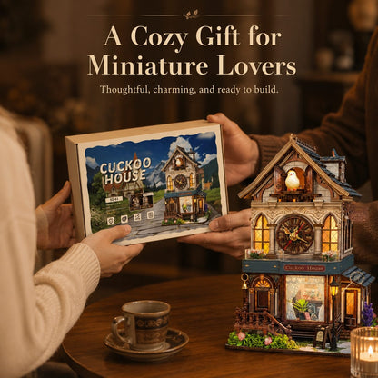 A cozy gift set featuring a miniature house model and its packaging box, held by two people in a warmly lit indoor setting. The box is labeled 'CUCKOO HOUSE,' and the assembled miniature house beside it is detailed with warm glowing lights, small figurines, and decorative elements.