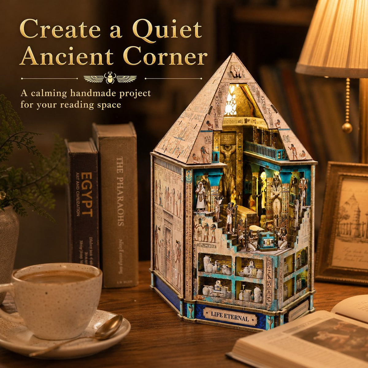 A handmade wooden miniature house book nook model with Egyptian-themed illustrations and interior scenes, displayed on a wooden table beside books, a coffee cup, and a lamp. Text on the image reads 'Create a Quiet Ancient Corner' and 'A calming handmade project for your reading space.