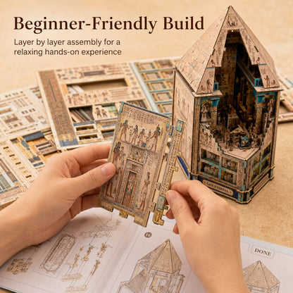A person's hands are shown assembling a wooden 3D model kit, holding a wooden panel with ancient Egyptian-style illustrations. In the background, a completed multi-level house model is displayed next to its instruction sheets on a beige surface.
