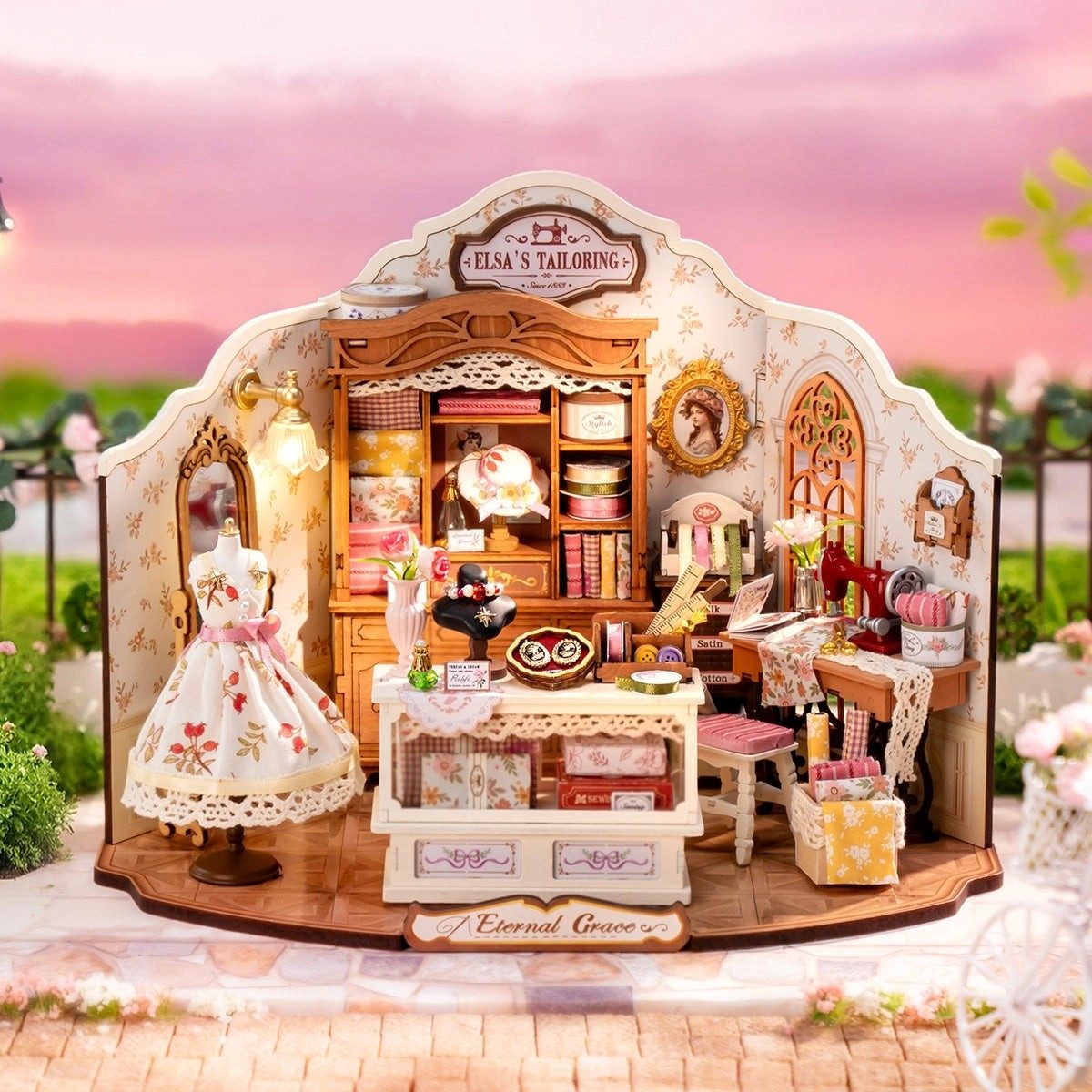 Miniature tailor shop model with detailed furniture and decor against a pink sky.