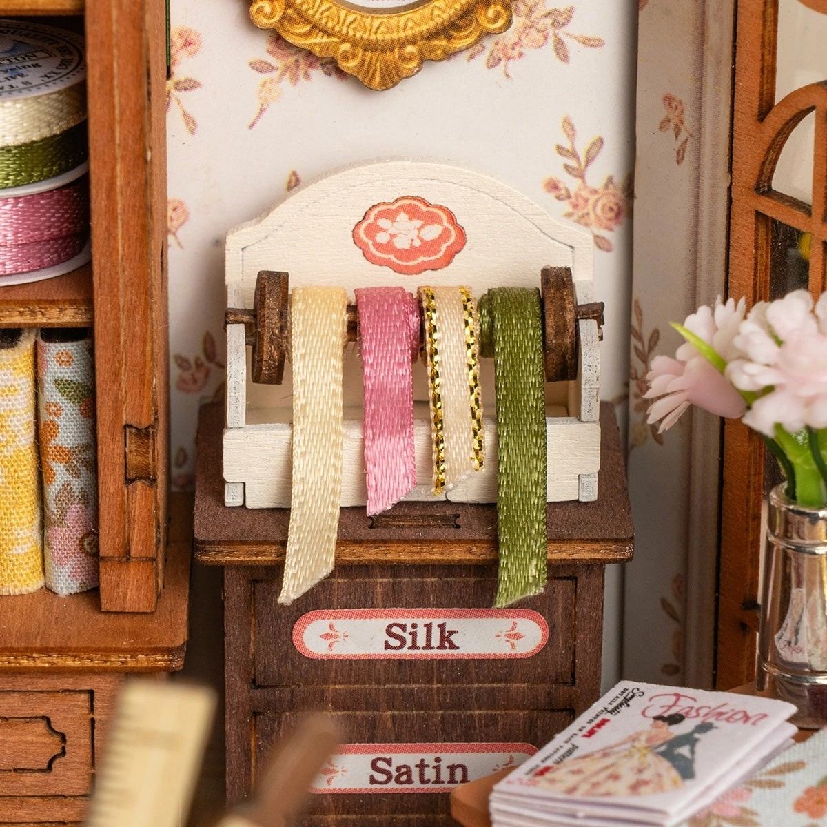 Miniature fabric display with spools of silk and satin in a decorative setting.