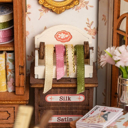 Miniature fabric display with spools of silk and satin in a decorative setting.