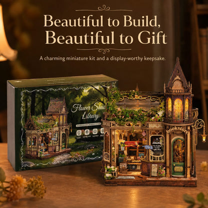 A decorative miniature library building kit shown next to its retail box on a wooden surface, with warm text above reading 'Beautiful to Build, Beautiful to Gift.' The product appears to be a detailed model kit with a fantasy forest-themed house, glowing windows, and small decorative elements.