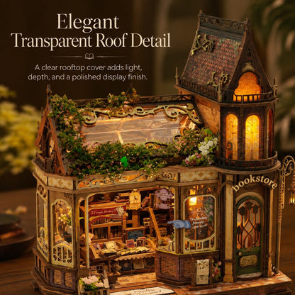 A decorative miniature house model with a transparent roof detail, shown in a warm, cozy interior scene. The building features a dark tiled roof, glowing yellow windows, greenery on the roof, and a storefront labeled 'bookstore' on the front.