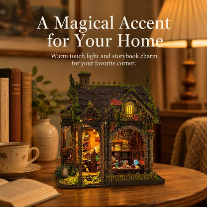 A miniature fairy light house with a dark gray roof, green mossy vines, and warm yellow glowing windows, displayed on a wooden table in a cozy room setting with books, a teacup, and a lamp in the background. Text overlay reads 'A Magical Accent for Your Home'.