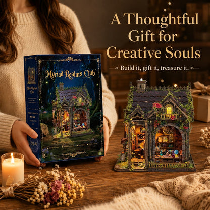 A cozy tabletop scene shows a person holding a decorative gift box labeled 'Myriad Realms Club' beside a fully built miniature house dollhouse with warm glowing windows. The scene includes a candle, dried flowers, knitted fabric, and overlaid text reading 'A Thoughtful Gift for Creative Souls' and 'Build it, gift it, treasure it.