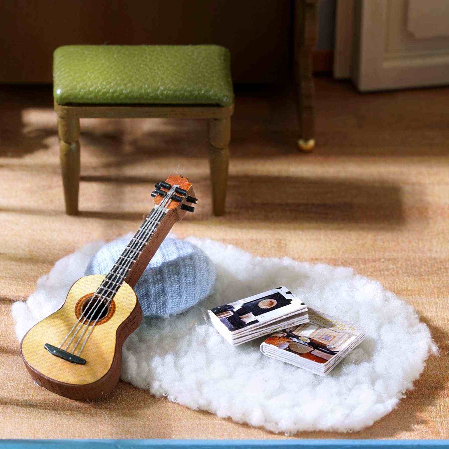 Small guitar on a fluffy white rug with magazines next to it, in a miniature room setting.