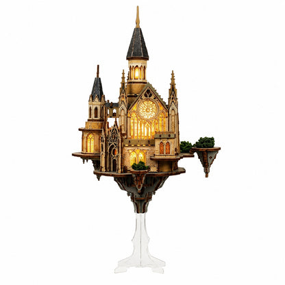 A detailed gothic castle miniature puzzle model on a clear acrylic stand, featuring warm yellow illuminated windows and dark gray roofs, set against a plain white background.