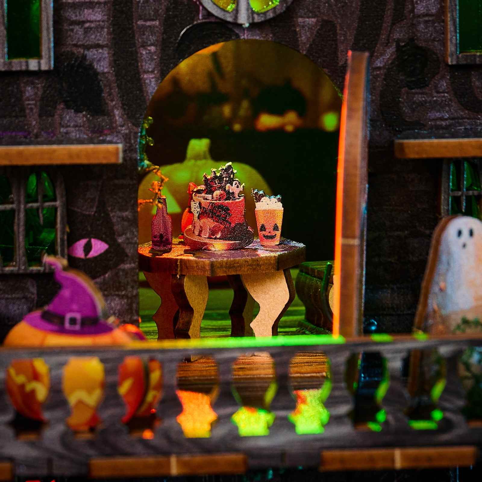 Halloween-themed diorama with a cake on a table, ghost, and pumpkins in a dark setting.