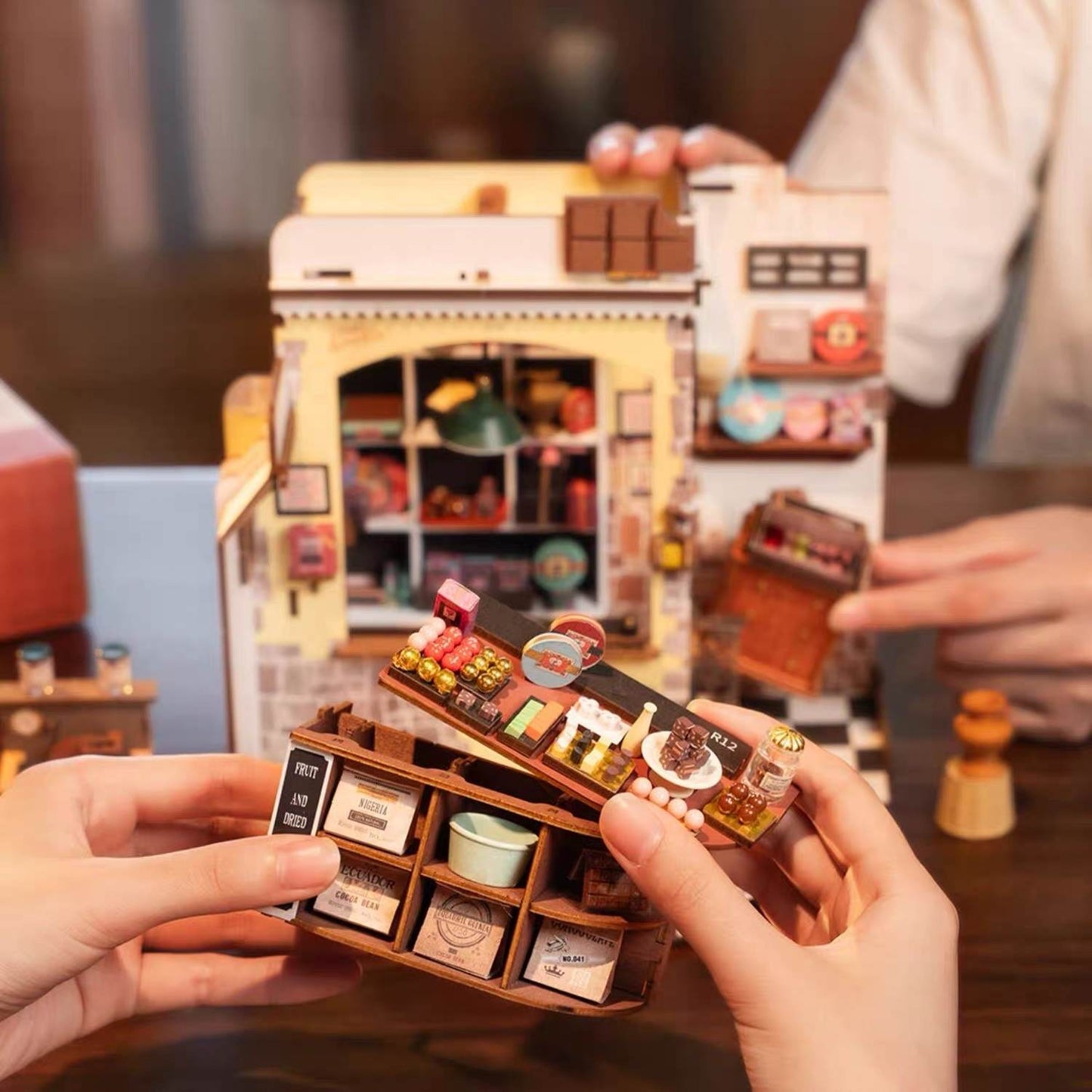 Close-up of hands holding a miniature model of a chocolate store