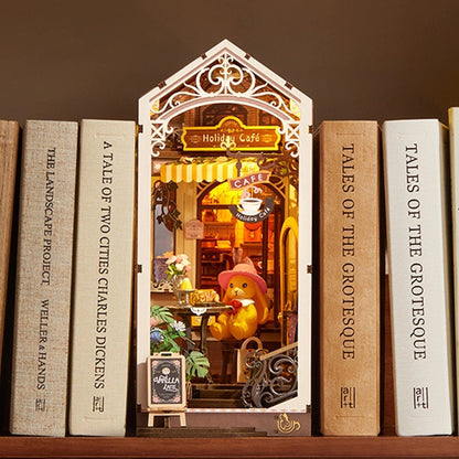Miniature cafe scene inside a bookshelf with books titled 'Tales of the Grotesque' and 'A Tale of Two Cities'.