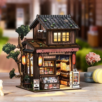 Wooden diorama model of a store with illuminated interior on a wooden surface.