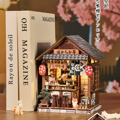 Miniature wooden Japanese Izakaya house with cherry blossom decorations next to books on a wooden surface.