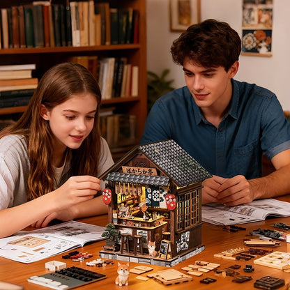 Two children assembling a detailed model of a Japanese Izakaya house at a table with books and building materials.