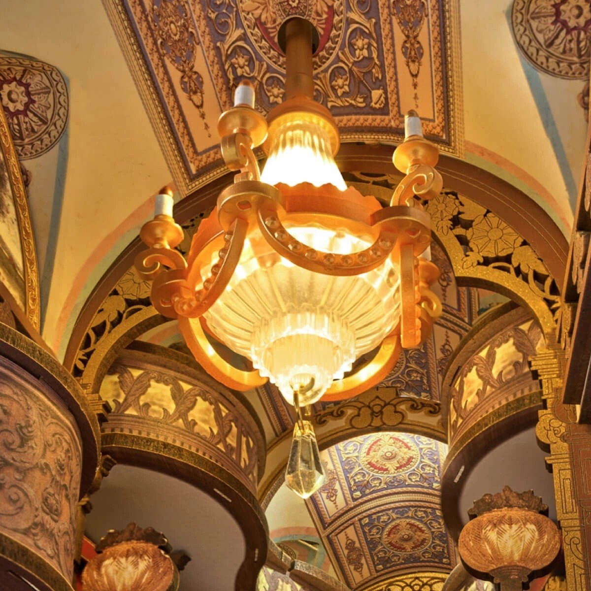 Decorative miniature vintage Baroque chandelier hanging from a ornate ceiling with intricate designs.