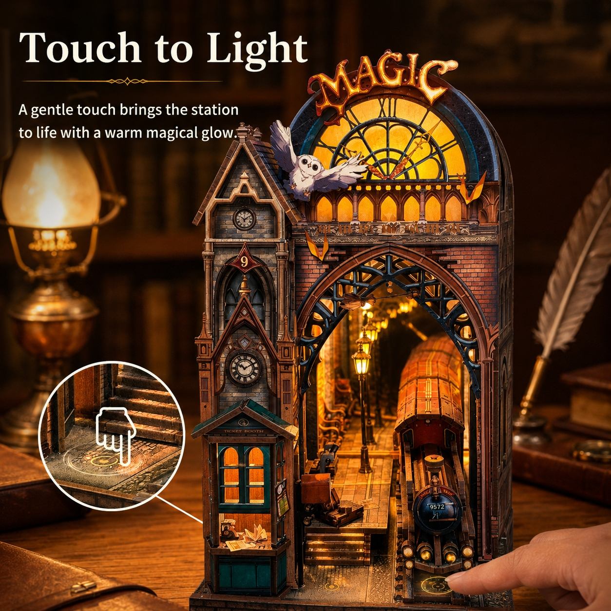 A 3D puzzle model of a magical vintage train station and locomotive, shown with a finger touching it to activate its warm glowing light feature. The scene is set on a wooden desk with a book and a feather quill in a cozy, dimly lit background.