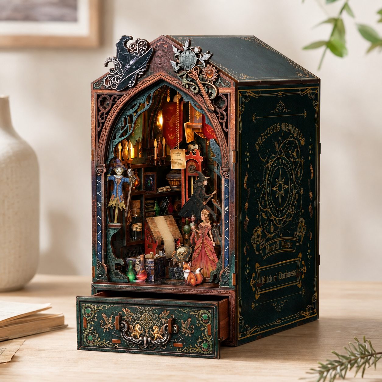 A miniature bookcase or music box with a dark green and bronze gothic design, featuring a detailed interior scene with candles, books, and small figurines, displayed on a wooden surface.