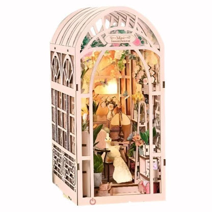 image displaying the finished Mini Greenhouse DIY Book Nook Kit, Featuring a light pink romantic design, lush plants, touch-activated lights, and easy assembly, it’s perfect as a gift or bookshelf décor.