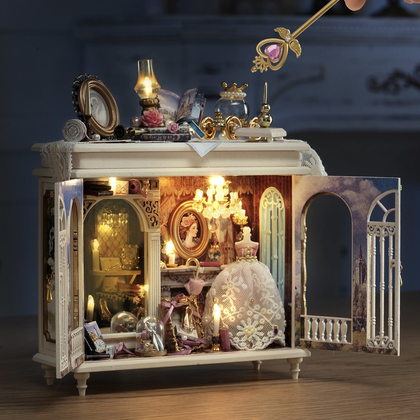 Decorative miniature scene with a chandelier, crown, and other ornaments inside a cabinet.