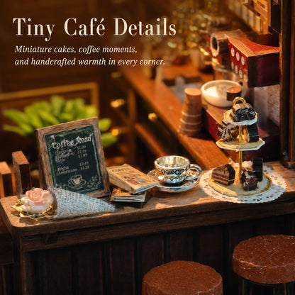 A miniature café display with tiny tabletop accessories including a small coffee menu sign, miniature teacups, a cup of tea on a saucer, pastries on a two-tier stand, and a small pink flower, set in a warm, cozy café scene with overlaid text reading 'Tiny Café Details'.