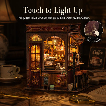 A miniature coffee shop night light with warm glowing interior lights, shown on a wooden table with coffee-themed props. Text at the top reads 'Touch to Light Up' with a circular inset showing the touch switch.