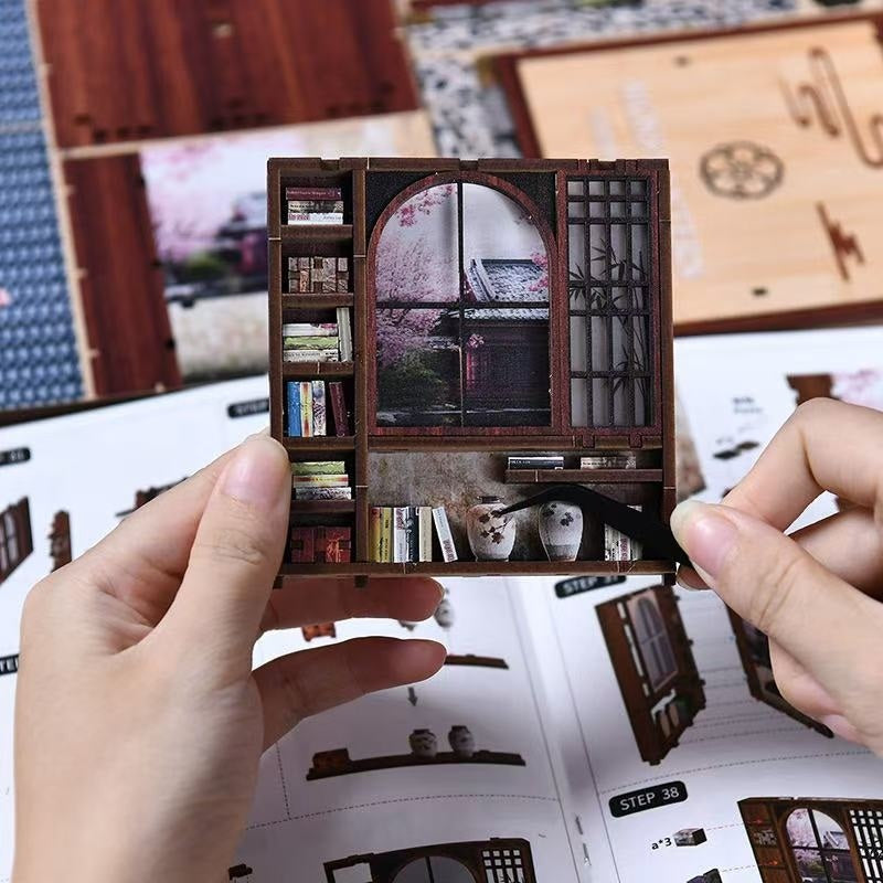 Miniature model of a bookshelf with books and decorative items, held by hands
