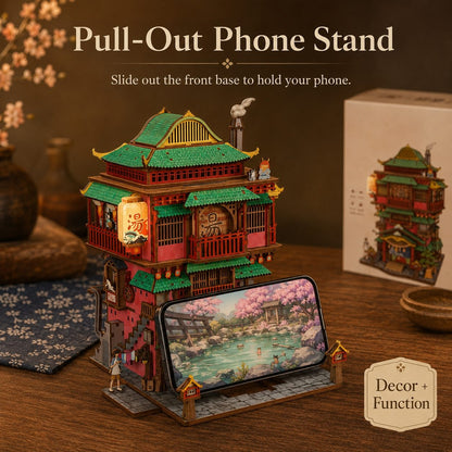 A decorative pull-out phone stand shaped like a traditional East Asian pagoda-style building, shown holding a smartphone on a wooden tabletop. The image includes text reading 'Pull-Out Phone Stand' and 'Decor + Function,' with the product box visible in the background.