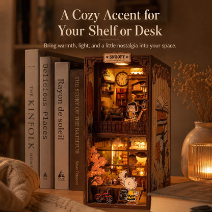 Decorative light-up miniature book nook with Snoopy and Woodstock, surrounded by books and a vase with dried flowers, on a shelf.